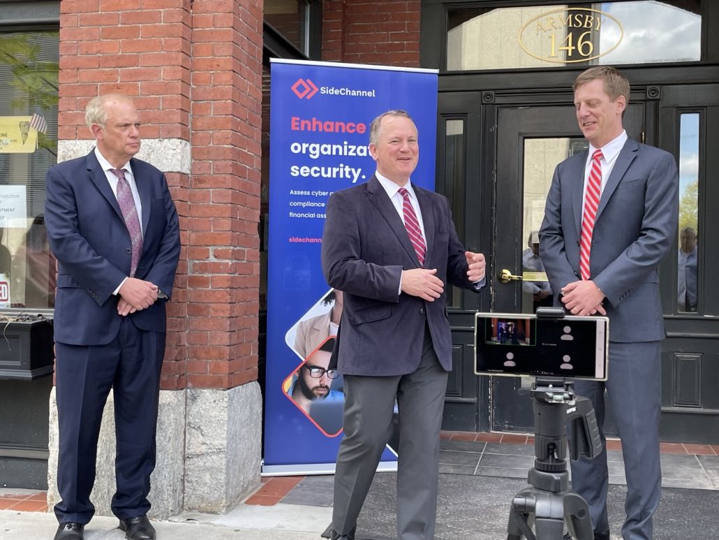 three men in dark blue suits stand in front of a red brick portico to commemorate an office opening