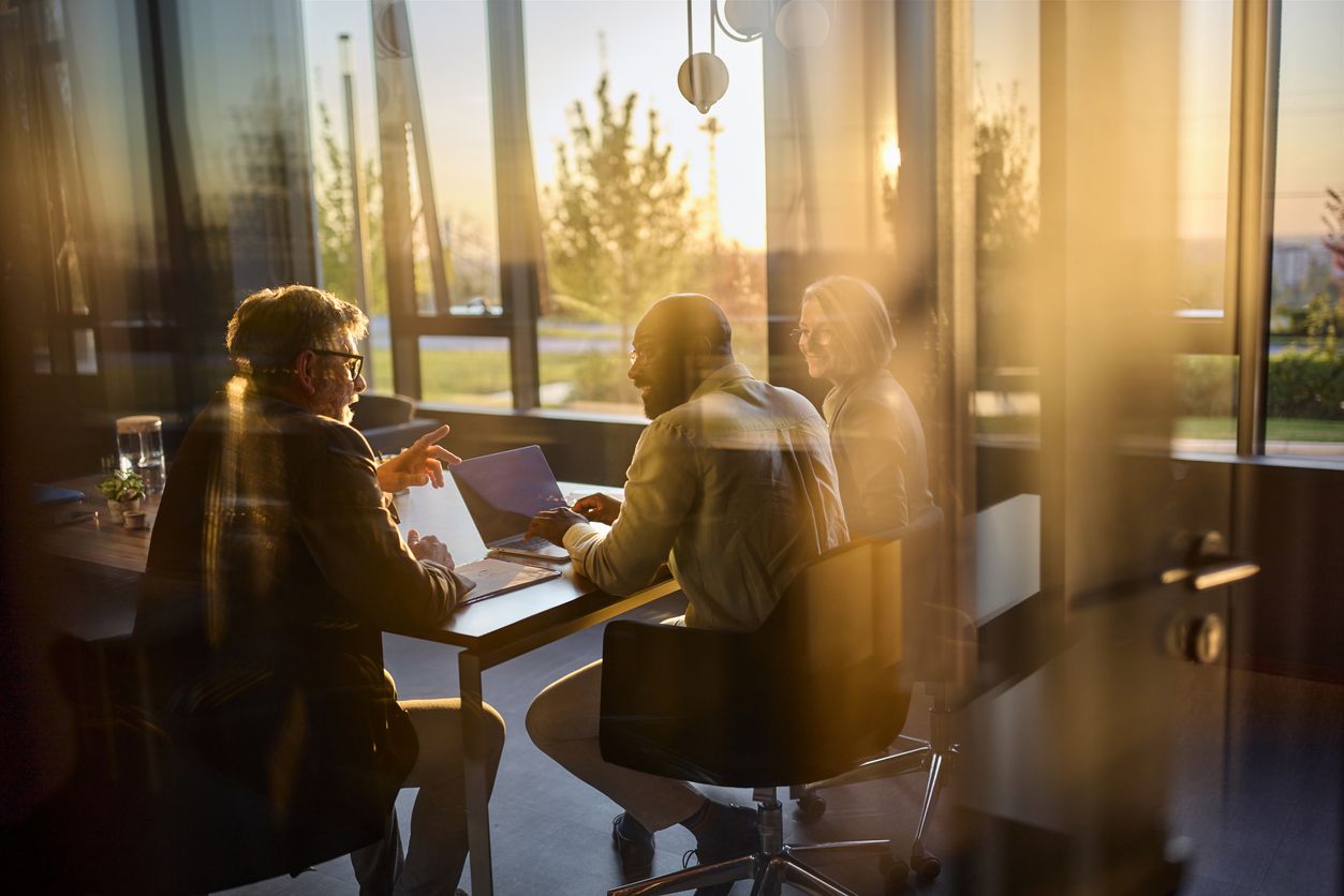 Business people collaborating on a laptop in a modern office during sunset.