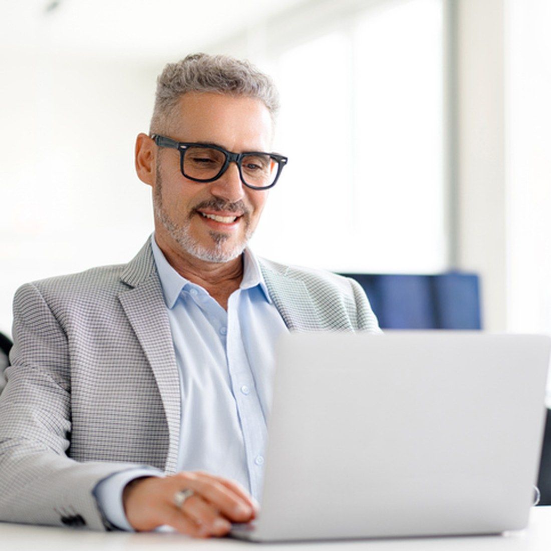 A professional man with glasses using a laptop in a bright, modern office setting.