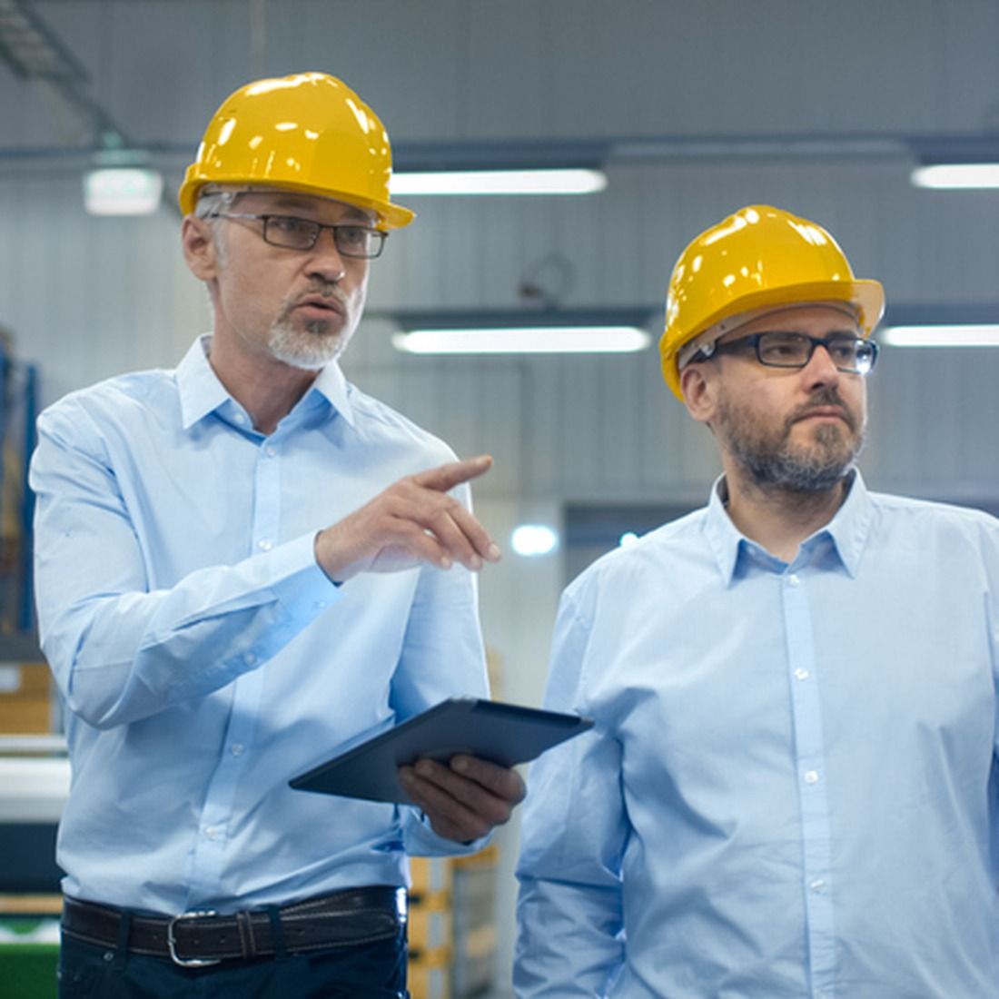 Two engineers wearing yellow safety helmets and glasses discuss critical infrastructure in an industrial facility.