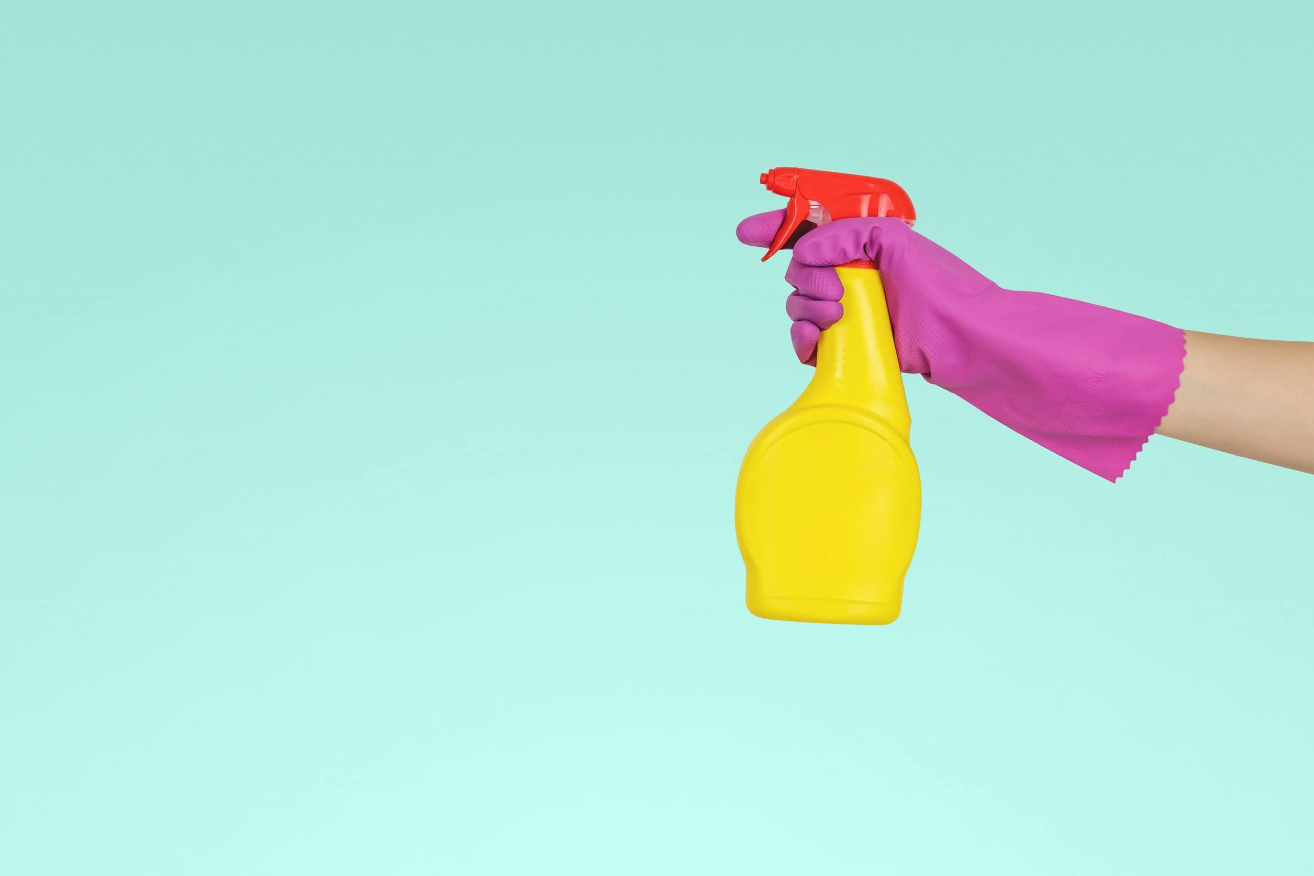 yellow spray bottle in a pink gloved hand on a periwinkle blue background