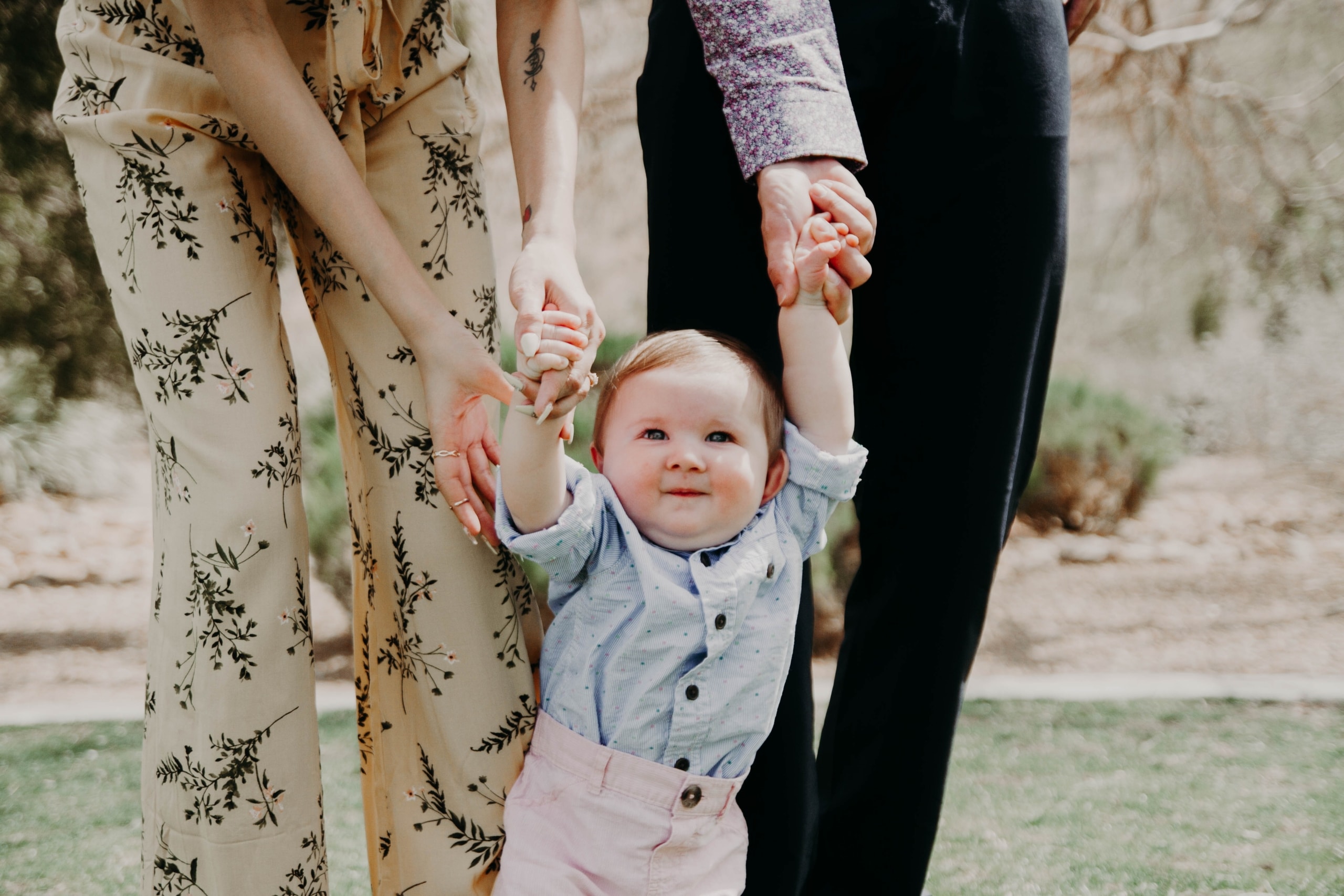 parents hold a baby's hands so it can walk upright