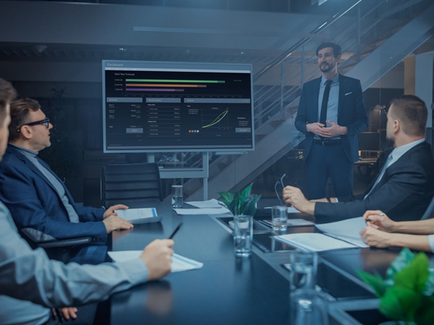 A businessman presents financial data on a screen to colleagues in a modern conference room.